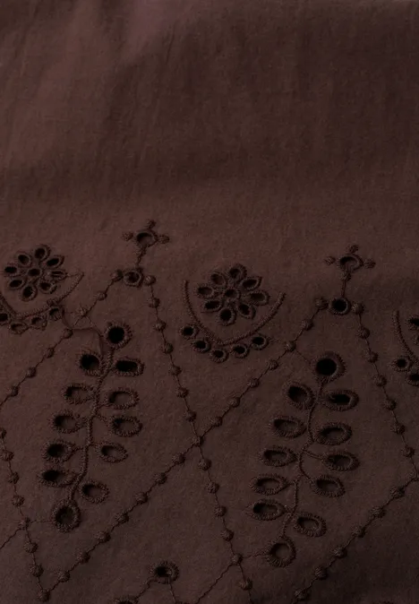 Close-up van een donkerbruin stof met fijn borduurwerk van bloemen- en bladvormen.