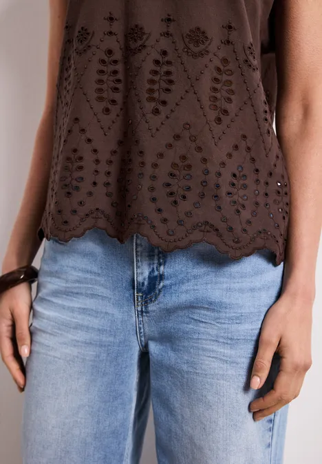 Iemand draagt een bruin topje met ajourdetails en een lichtblauwe jeans.