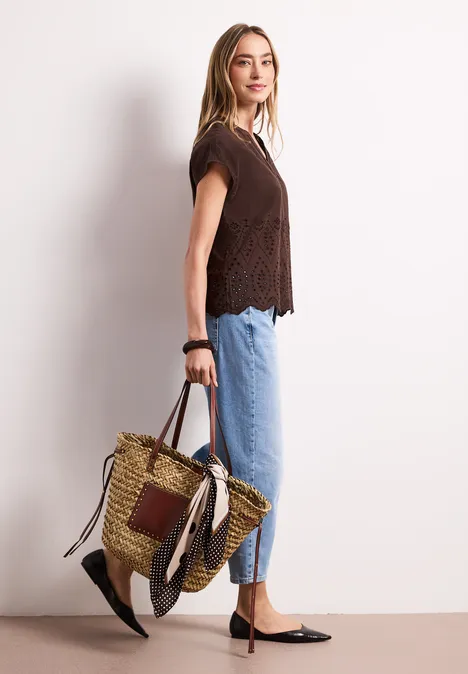 Vrouw in profiel met kanten top, blauwe jeans, zwarte ballerina’s en een gevlochten strozak.