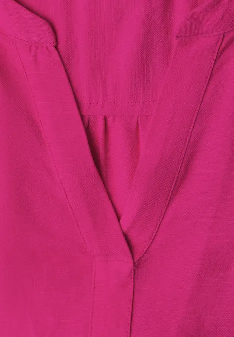 Nahaufnahme eines knallpinken Kleidungsstücks mit sichtbarer Naht am V-Ausschnitt.