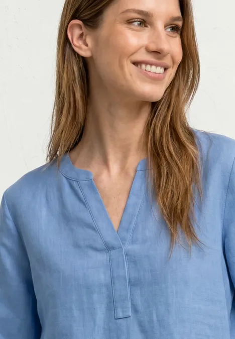 Person trägt hellblaue Bluse mit V-Ausschnitt, Gesicht unscharf, neutraler Hintergrund.