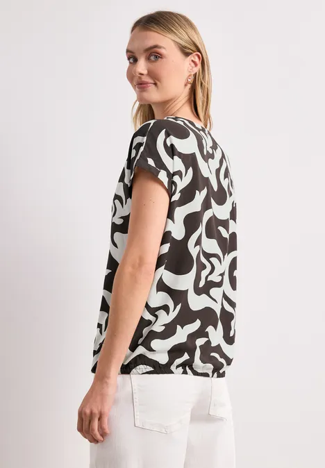 Profil d'une femme portant un t-shirt à motifs noirs et blancs à manches courtes et un pantalon blanc.