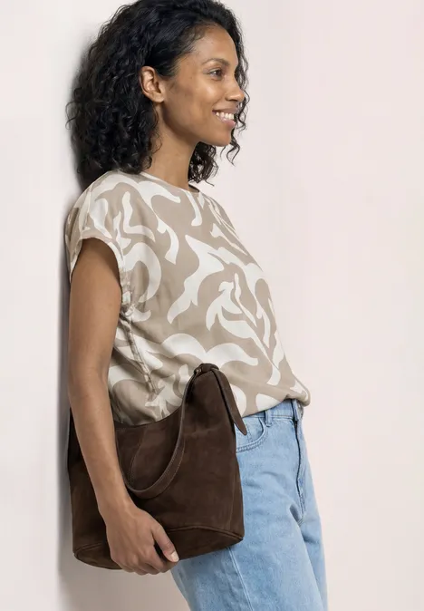 Frau im Profil mit gemustertem T-Shirt, Jeans und brauner Schultertasche.