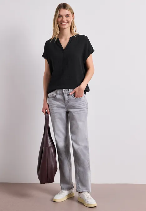 Frau trägt schwarzen V-Ausschnitt-Shirt, graue Baggy-Jeans, weiße Sneaker und hält eine große bordeauxrote Tasche.