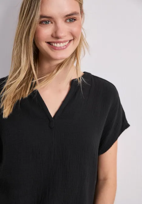 Frau in locker sitzendem, schwarzem V-Ausschnitt-Shirt vor weißem Hintergrund.