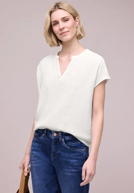 Frau trägt weiße Bluse, blaue Jeans und hält lässig eine braune Handtasche.