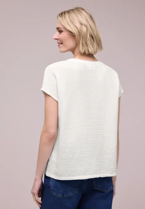 Frau von hinten in weißem kurzärmeligem Oberteil und Jeans vor neutralem Hintergrund.