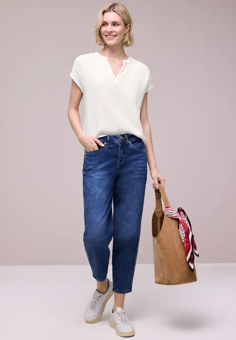 Frau trägt weißes Shirt, blaue Jeans, weiße Sneaker und hält Strohtasche mit rotem Tuch.