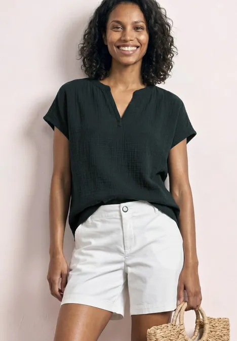 Frau trägt schwarze Bluse, weiße Shorts und hält eine Strohtasche.