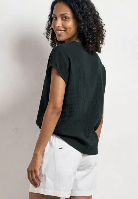 Person mit lockigen Haaren trägt schwarzes Shirt und weiße Shorts, steht seitlich mit dem Rücken zur Kamera.