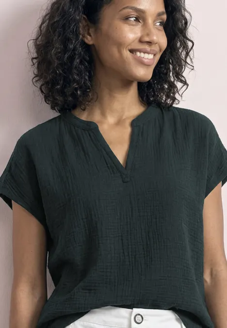 Eine lächelnde Frau mit lockigen Haaren trägt eine schwarze Bluse vor rosa Hintergrund.