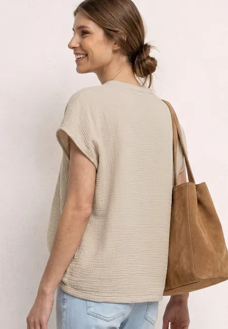 Frau trägt hellbeige, ärmelloses T-Shirt und eine braune Wildleder-Tasche, Rückenansicht.