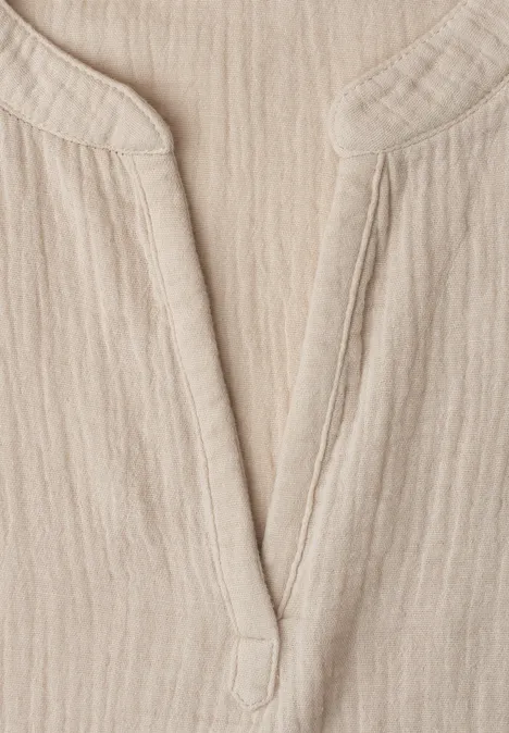 Nahaufnahme eines hellbeigen, gerippten Leinenstoffs mit V-Ausschnitt eines Hemdes oder Kleids.