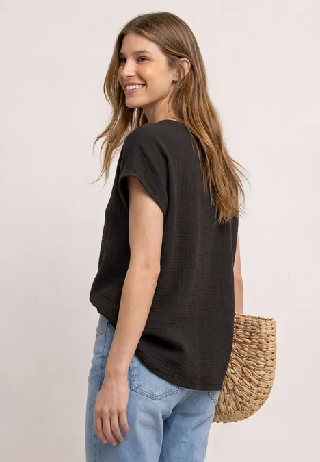 Frau in schwarzem T-Shirt und blauen Jeans, seitlich fotografiert, mit einer Strohtasche.