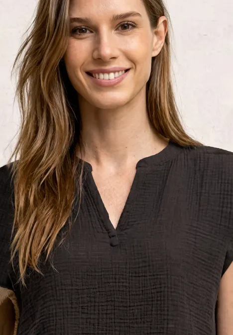 Frau mit langem braunem Haar trägt schlichte schwarze, strukturierte Bluse mit V-Ausschnitt.