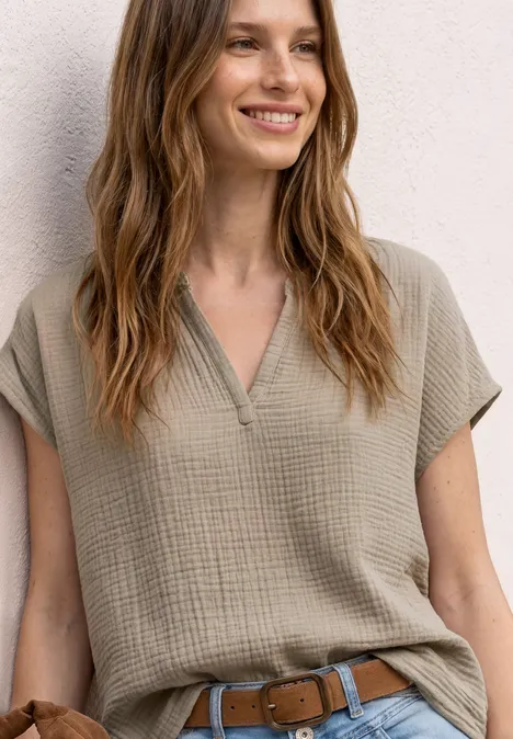 Frau trägt khakifarbenes, kurzärmeliges V-Shirt mit Gürtel und weicher Struktur.