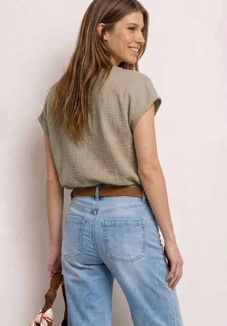 Rückansicht einer Frau in lockeren Jeans, kurzem Oberteil und braunem Gürtel, die eine Tasche an der Seite hält.