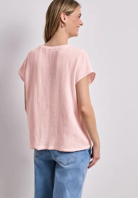 Rückenansicht einer Frau in lockerem rosa T-Shirt und blauen Jeans vor weißem Hintergrund.