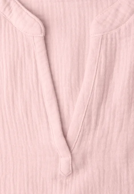 Nahaufnahme eines rosa Hemdes aus leichtem Stoff mit V-Ausschnitt und dekorativem Knopfdetail.