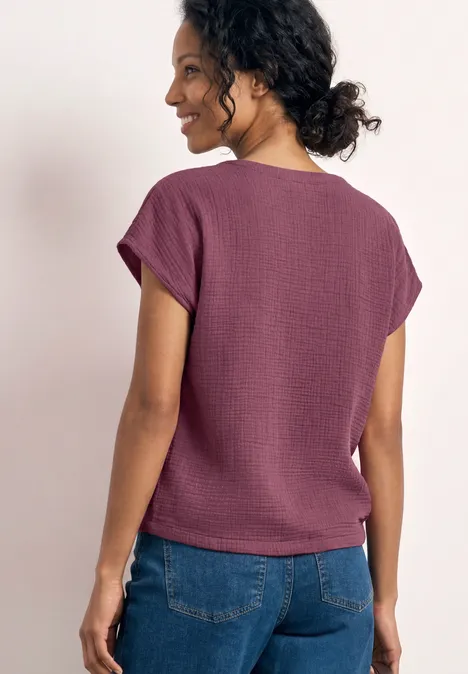 Frau von hinten in lila T-Shirt mit Kurzarm und blauen Jeans.