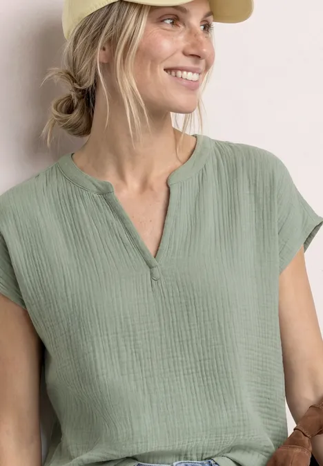 Frau in lockerem, hellgrünem Baumwollshirt mit kurzen Ärmeln und kleinem V-Ausschnitt.