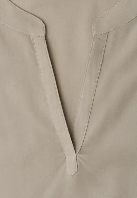 Nahaufnahme eines hellbeigen Baumwollshirts mit V-Ausschnitt und feiner Naht.