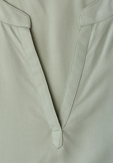 Nahaufnahme eines hellgrünen Kleidungsstücks mit V-förmigem Ausschnitt und minimalistischem Design.