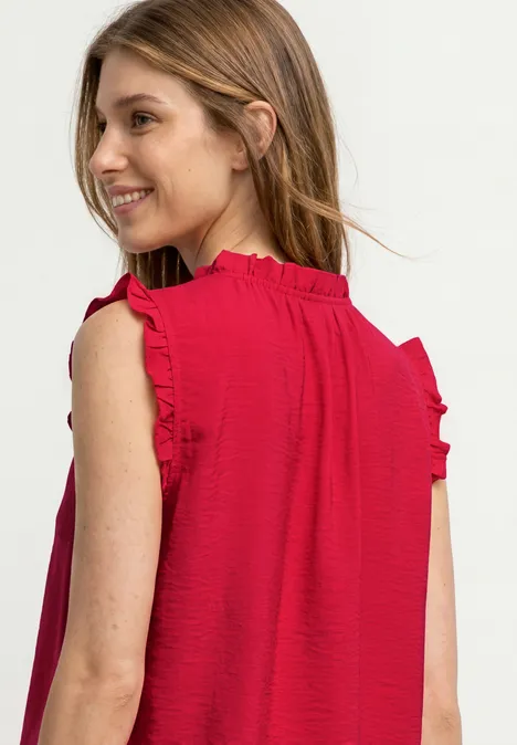 Ein Mädchen von hinten in rotem ärmellosem Kleid mit Rüschen an den Schultern.