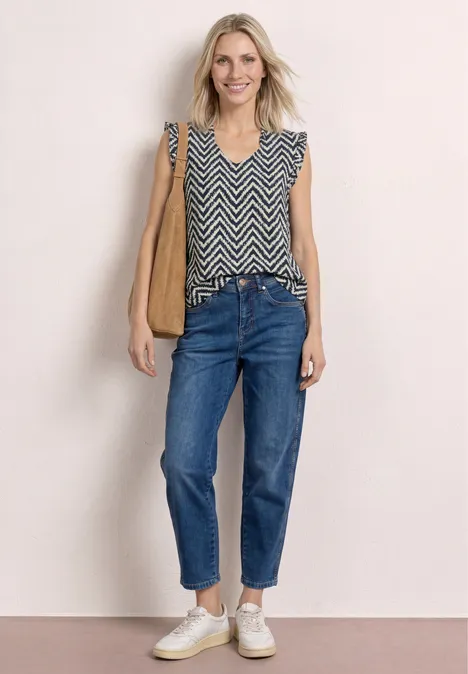 Frau in ärmellosem Zickzack-Top, Jeans, weiße Sneakers, braune Schultertasche
