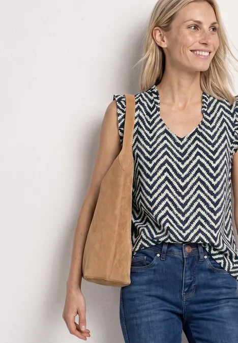 Frau in schwarz-weißem Zickzack-Top, Jeans und brauner Stofftasche