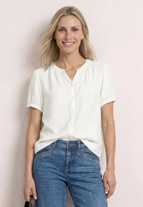 Frau in weißer Bluse und blauen Jeans vor hellem Hintergrund.
