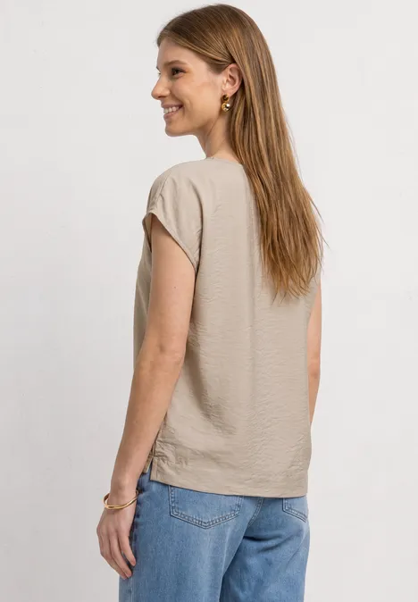 Frau von hinten in beigem T-Shirt und blauen Jeans vor weißem Hintergrund.