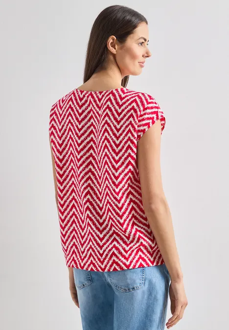 Frau von hinten in rotem Zickzack-Shirt und blauen Jeans.