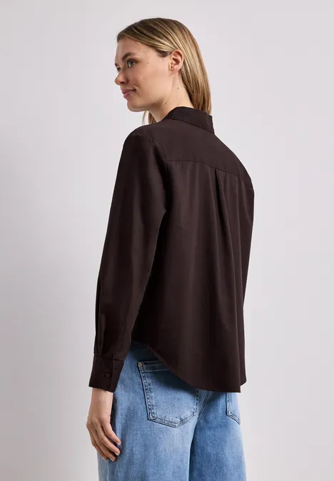 Frau von hinten mit schwarzem Hemd und blauer Jeanshose vor hellem Hintergrund.