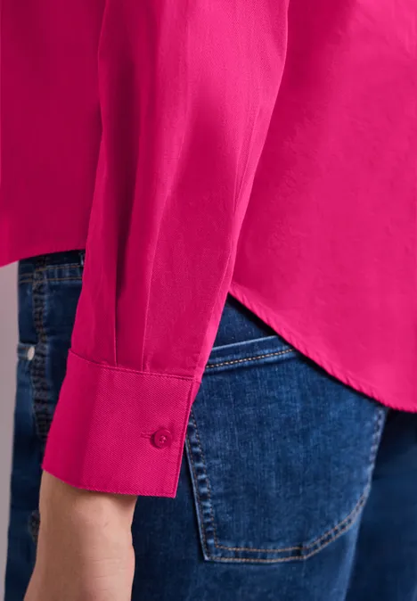 Zijaanzicht van een felroze blouse gedragen over een blauwe spijkerbroek.