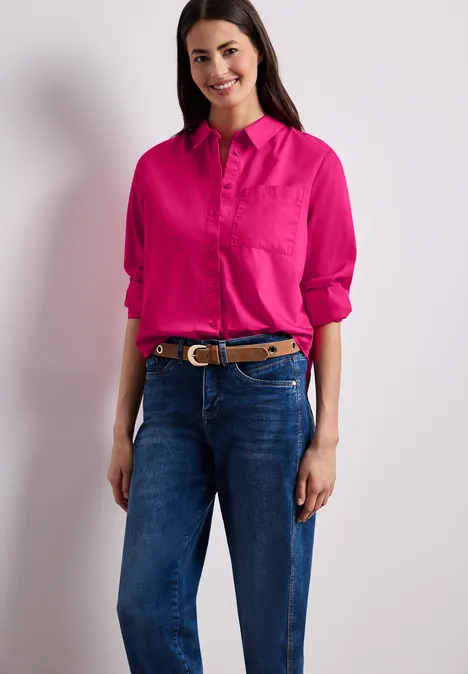 Een persoon draagt een felroze blouse en een blauwe jeans voor een witte achtergrond.