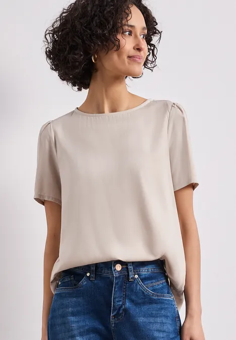 Een vrouw draagt een crème korte mouwen blouse en blauwe jeans tegen een lichte achtergrond.