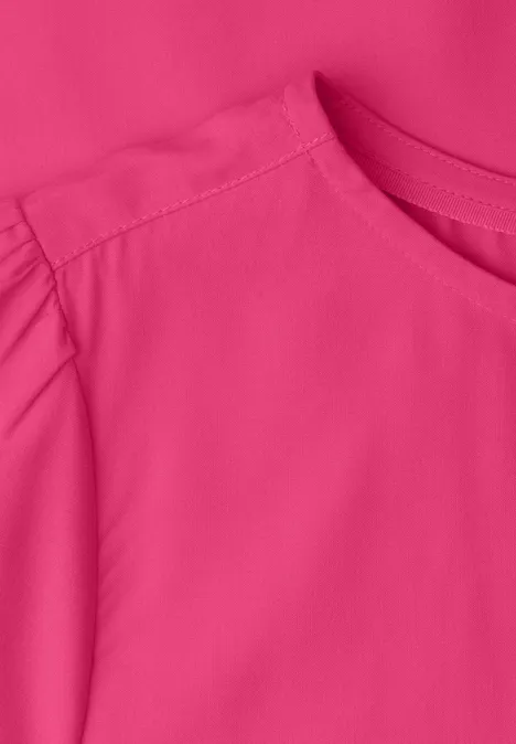 Close-up van een felroze top met ronde hals en geplooide mouw.