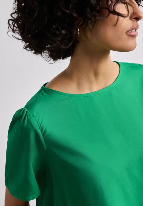 Bluse mit Rundhals und kurzen Puffärmeln ever green Eine Person trägt eine grüne Bluse mit kurzen Ärmeln, Blick seitlich.