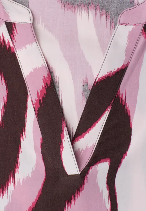Close-up van een kledingstuk met V-hals en abstract patroon in roze, wit en bruin.