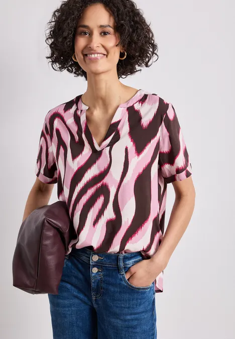 Vrouw in jeans en kortemouwshirt met roze-zwarte print, draagt een bordeauxrode tas.