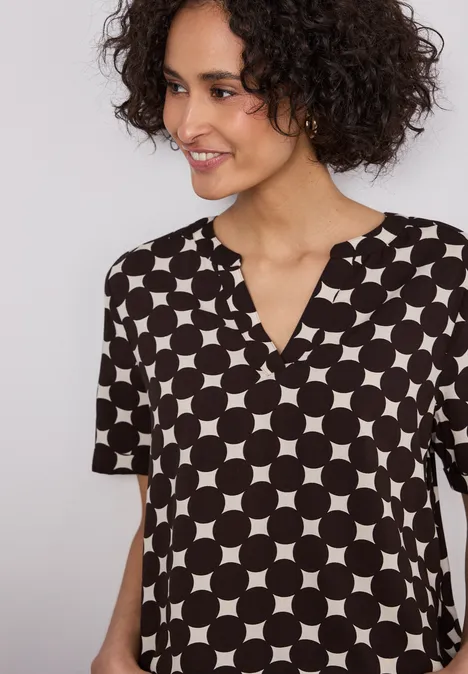 Een persoon draagt een zwart blouseje met korte mouwen en een patroon van witte cirkels.