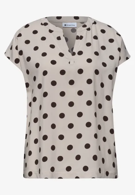 Beige blouse met zwarte polkadots en korte mouwen.