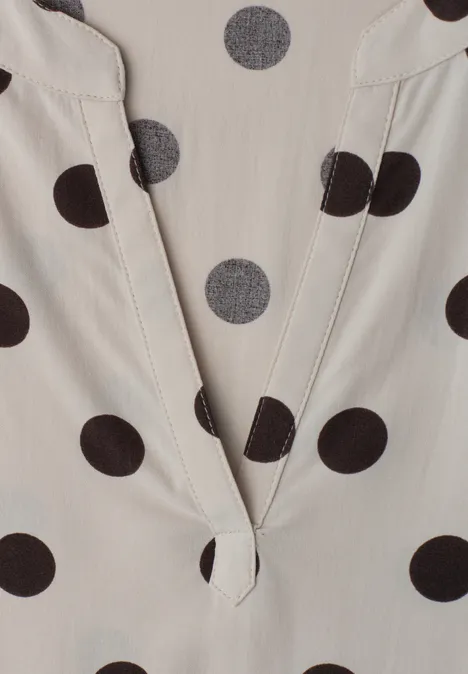 Close-up van een lichtbeige top met zwarte polka dots en V-hals.