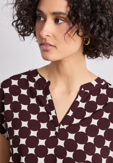 Dropped Shoulder Bluse mit Split Neck rustic rouge Porträt einer Frau mit dunklen Locken in einem weißen Top mit großen dunkelbraunen Punkten.