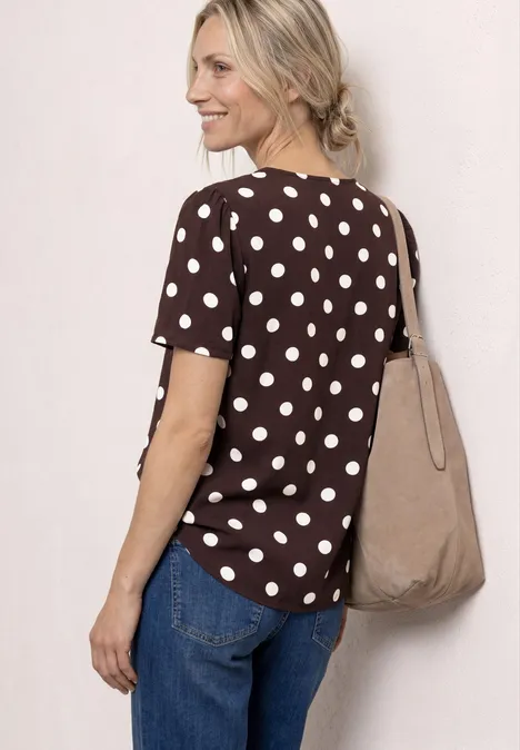 Frau von hinten in braunem Tupfen-Shirt, blauen Jeans und beiger Stofftasche.