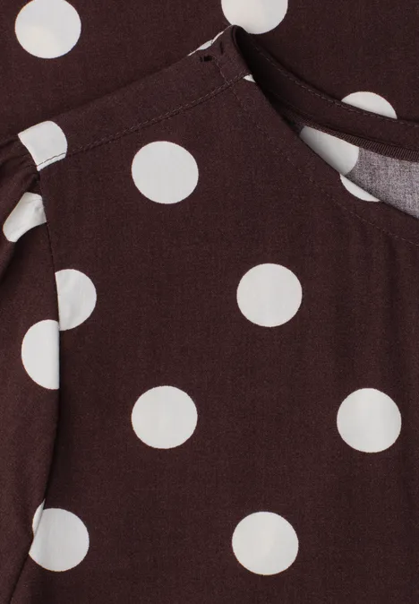 Brauner Stoff mit großen weißen Punkten und einer Naht, vermutlich Teil eines Kleidungsstücks mit Tasche.