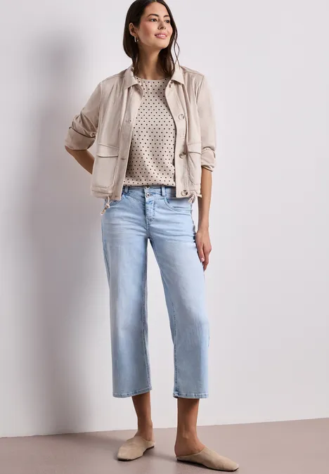 Frau trägt beige Jacke, gemusterten Pullover, hellblaue Cropped-Jeans und beigen Mules.