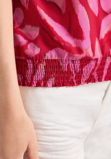 Nahaufnahme: Rotes, gemustertes Top und weiße Hose.