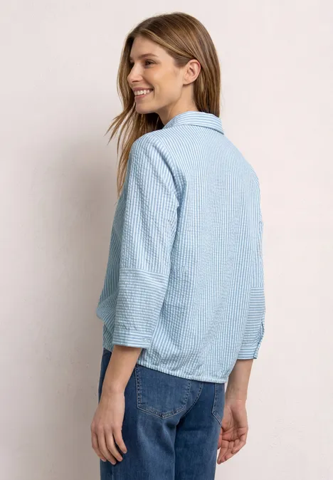 Rückansicht einer Frau in hellblau gestreiftem Hemd mit hochgekrempelten Ärmeln und Jeans.